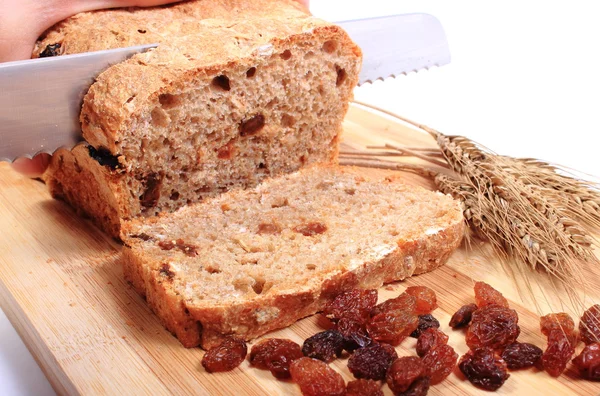 Rebanando pan fresco, espigas de trigo y pasas — Foto de Stock