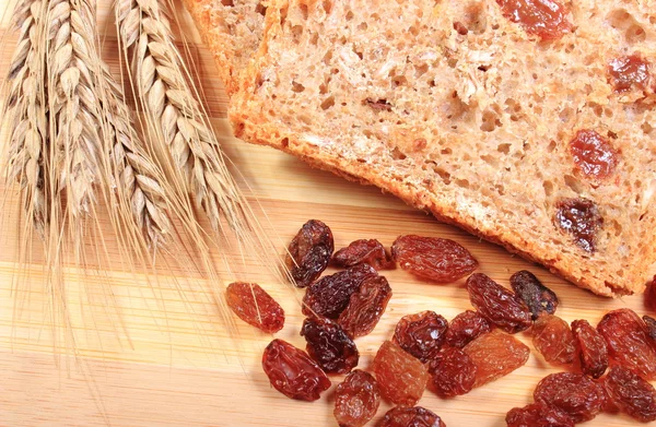 Fresh baked bread, ears of wheat and raisins — Stock Photo, Image