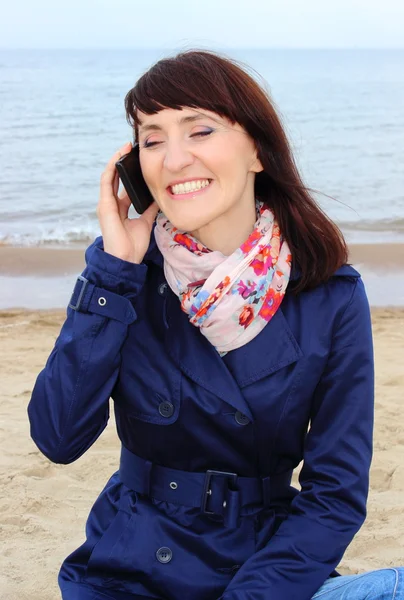 Vrouw met mobiele telefoon zittend op het strand — Stockfoto