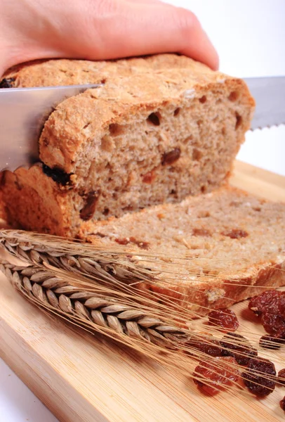 Rebanando pan fresco, espigas de trigo y pasas — Foto de Stock