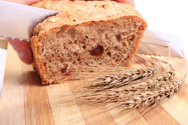 Mano de mujer rebanando pan fresco, espigas de trigo — Foto de Stock