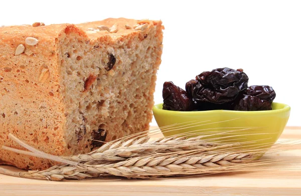 Pão integral assado, ameixas secas e espigas de trigo — Fotografia de Stock