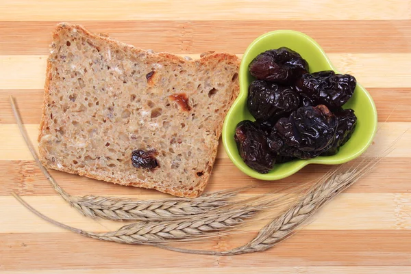 Gebakken volkoren brood, gedroogde pruimen en oren van tarwe — Stockfoto