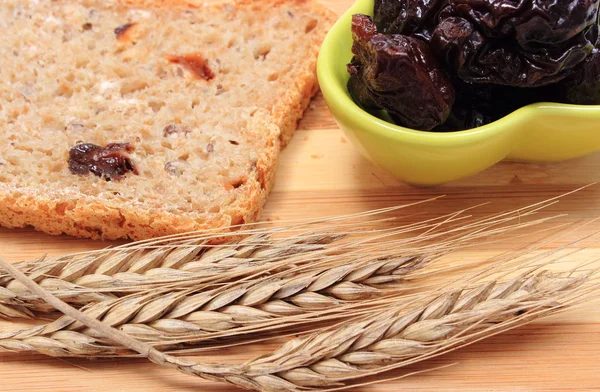 Baked wholemeal bread, dried plums and ears of wheat — Stock Photo, Image