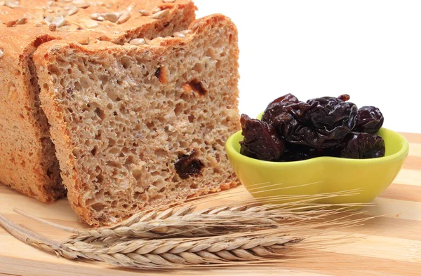 Baked wholemeal bread, dried plums and ears of wheat — Stock Photo, Image