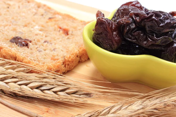 Baked wholemeal bread, dried plums and ears of wheat — Stock Photo, Image