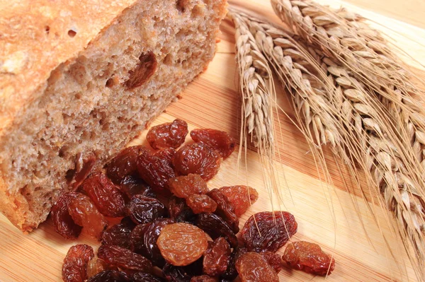 Pão integral assado, passas e espigas de trigo — Fotografia de Stock