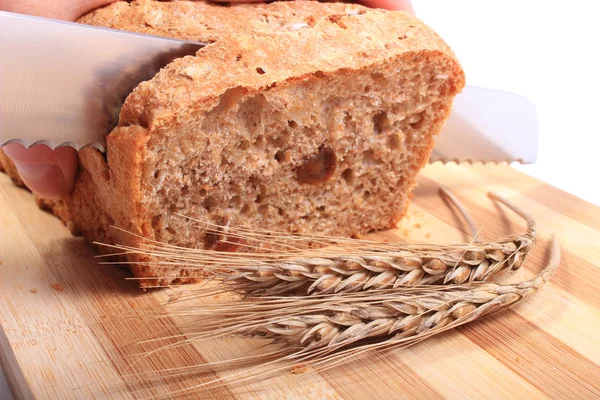 Hand of woman slicing fresh bread, ears of wheat — Stock Photo, Image