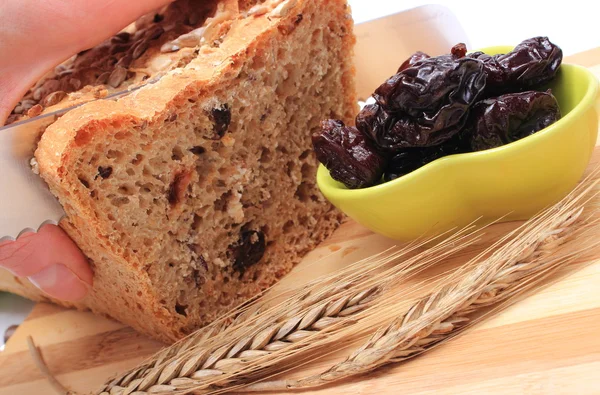 Slicing fresh bread, dried plums and ears of wheat — Stock Photo, Image