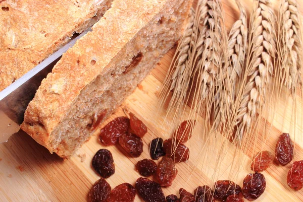 Slicing fresh bread, ears of wheat and raisins — Stock Photo, Image