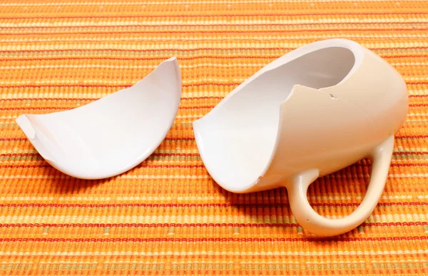 Разбитая кружка, разбитая чашка на оранжевой ткани — стоковое фото