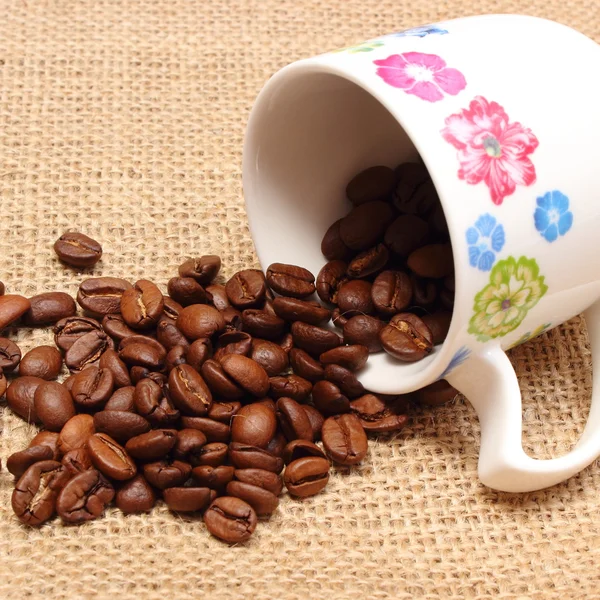 Куча зерна кофе с опрокинутой чашкой — стоковое фото