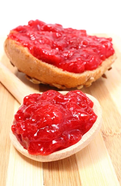 Strawberry jam on wooden spoon and whole wheat bread — Stock Photo, Image