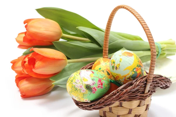 Цветные пасхальные яйца в плетеной корзине и свежие тюльпаны — стоковое фото