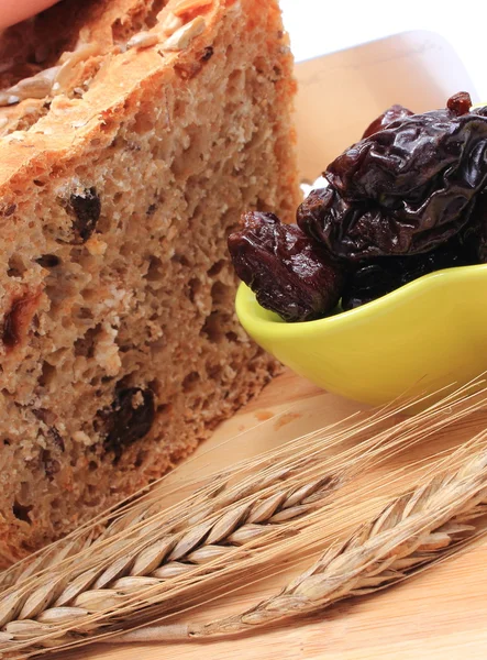 Snijden van vers brood, gedroogde pruimen en oren van tarwe — Stockfoto