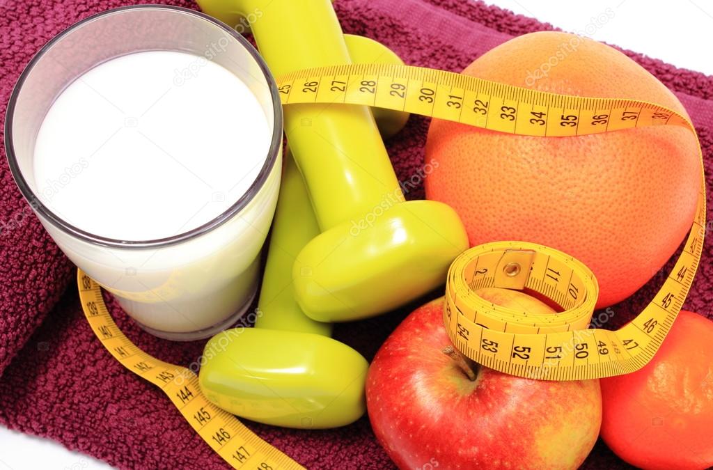 Fresh fruits, tape measure, milk and dumbbells on purple towel