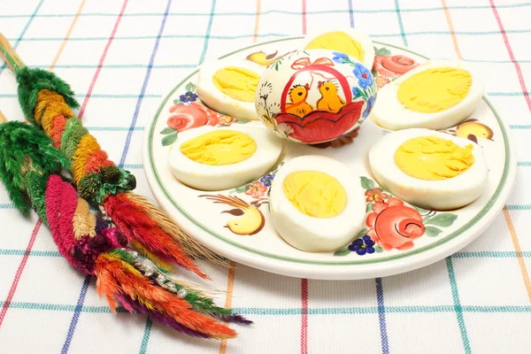 Easter palm, halves of eggs and painted egg on colorful plate — Stock Photo, Image