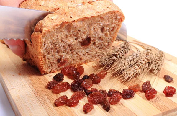 Slicing fresh bread, ears of wheat and raisins — Stock Photo, Image