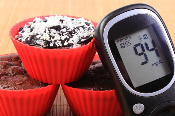 Glucose meter and chocolate muffins in red cups — Stock Photo, Image