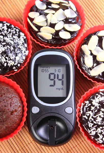Glucometer and chocolate muffins in red cups — Stock Photo, Image
