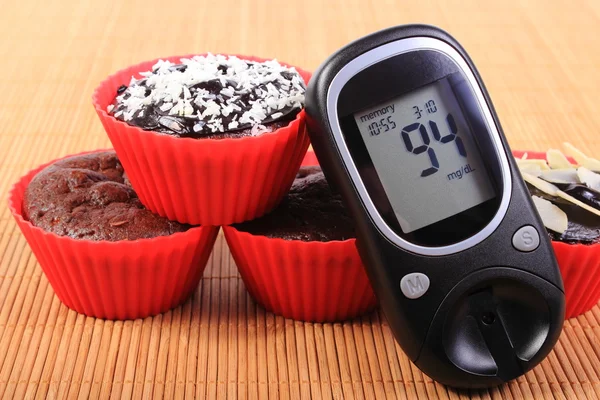 Glucometer and chocolate muffins in red cups — Stock Photo, Image