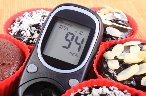 Medidor de glucosa y magdalenas de chocolate en tazas rojas — Foto de Stock