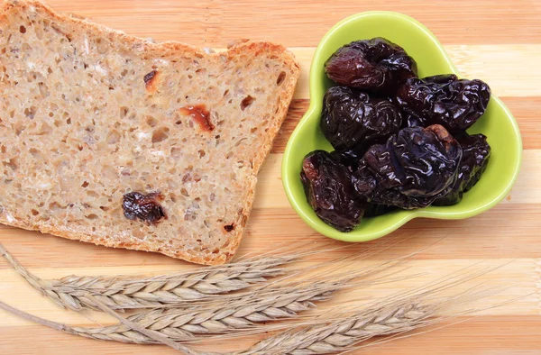 Gebakken volkoren brood, gedroogde pruimen en oren van tarwe — Stockfoto