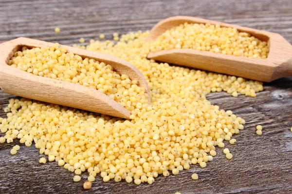 Heap of millet groats with spoon on wooden background — Stock Photo, Image