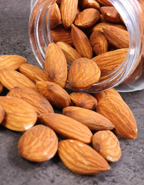 Almonds spilling out of glass jar on concrete structure — Stock Photo, Image