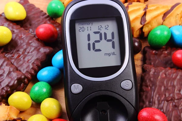 Medidor de glucosa con un montón de dulces, diabetes y alimentos poco saludables — Foto de Stock