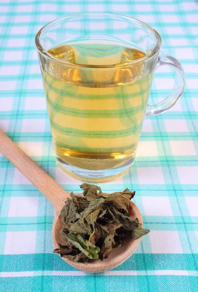 Mélisse séchée avec cuillère et verre de boisson aux herbes sur la nappe — Photo