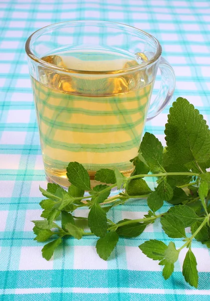 Fresh lemon balm and glass of herbal drink on tablecloth — Stockfoto