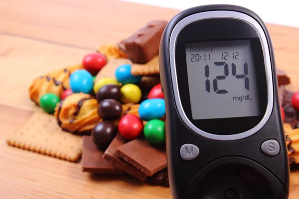 Глюкометр с кучей сладостей на деревянной поверхности, сахарным диабетом и нездоровой пищей — стоковое фото