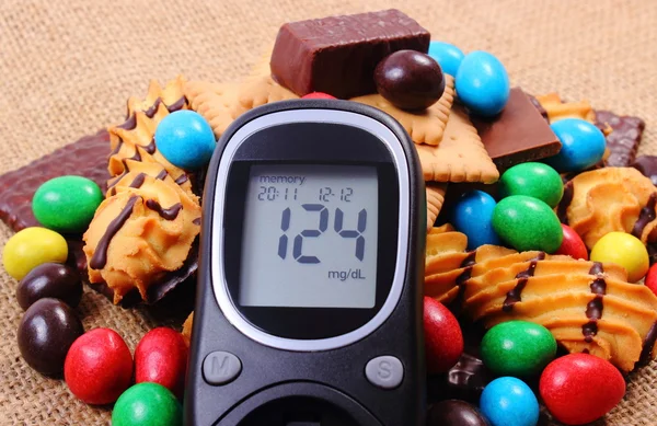 Glucometer con un montón de dulces en la arpillera del yute, diabetes y alimentos poco saludables — Foto de Stock