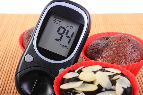 Glucometer and chocolate muffins in red cups — Stock Photo, Image