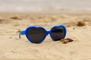 Mavi güneş gözlüğü kum üzerinde kabukları ile kalp şeklinde