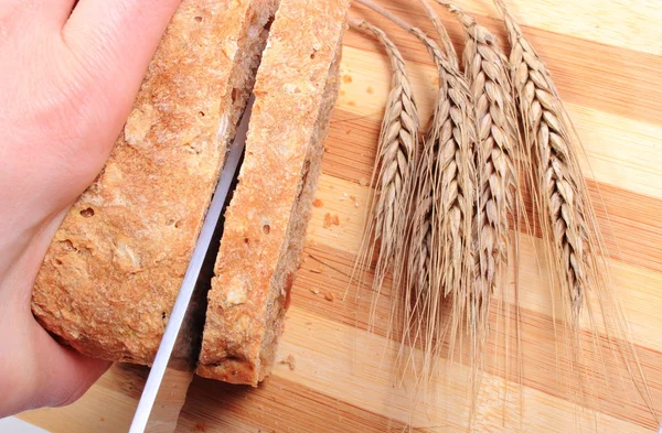 Mão de mulher cortando pão fresco, espigas de trigo — Fotografia de Stock