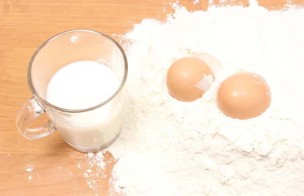 Harina de trigo, vaso de leche y dos huevos en la mesa —  Fotos de Stock