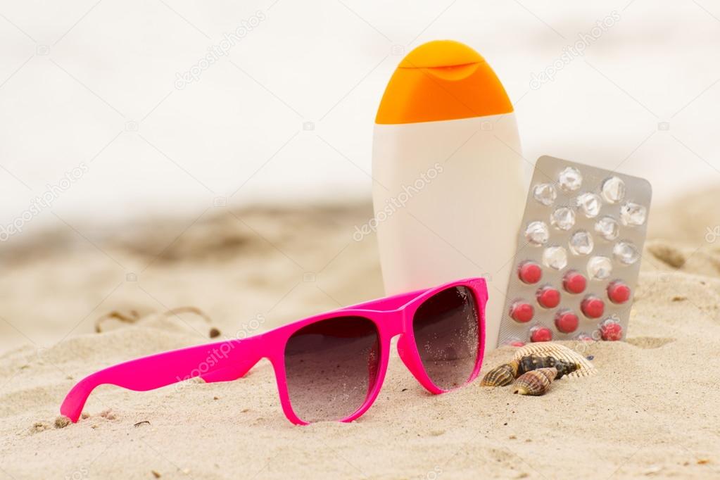 Pink sunglasses, shells, lotion and pills of vitamin A, seasonal concept