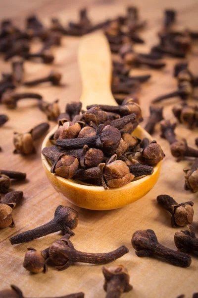 Cumulo di chiodi di garofano con cucchiaio di legno sulla tavola, condimento per cucinare — Foto Stock