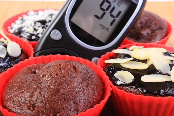 Glucometer and chocolate muffins in red cups — Stock Photo, Image