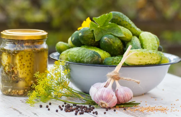 Cucumbers in metal bowl, spices for pickling and jar pickled cucumbers on table — Stock Photo, Image