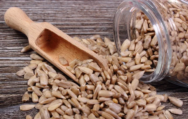 Zonnebloempitten morsen uit glazen pot. Houten achtergrond — Stockfoto