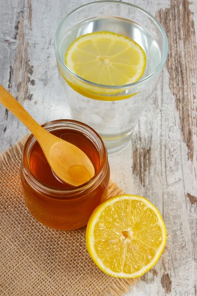 Свежий лимон с медом и стакан воды с ломтиком лимона — стоковое фото