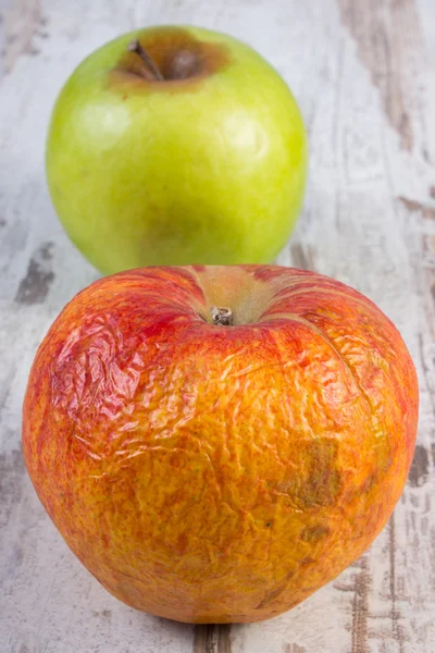 Spoiled apple on old wooden white table — Stock Photo, Image