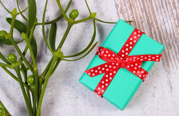 Wrapped green gift for Christmas and mistletoe on old wooden background — Stock Photo, Image