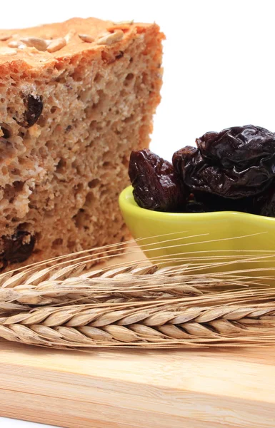 Pão integral assado, ameixas secas e espigas de trigo — Fotografia de Stock