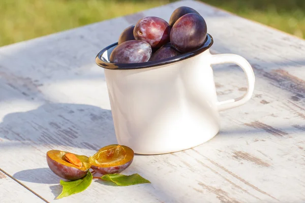 Heap of plums in metallic mug on wooden table in garden on sunny day — Stockfoto