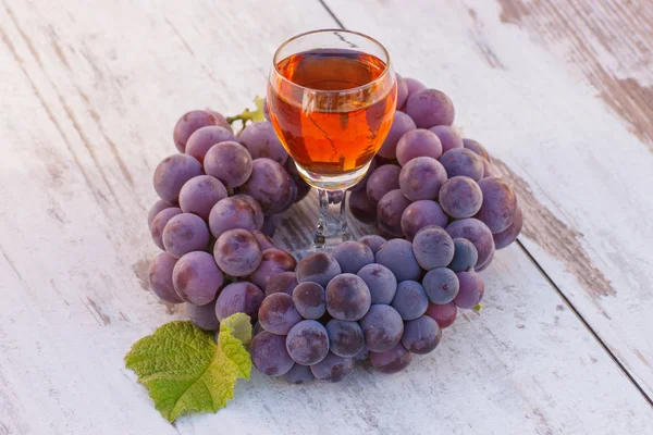 Grapes with leaf and glass of wine on wooden table in garden — Stock Photo, Image