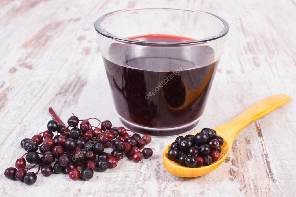 Fresh elderberry with wooden spoon and juice on old wooden background, healthy nutrition